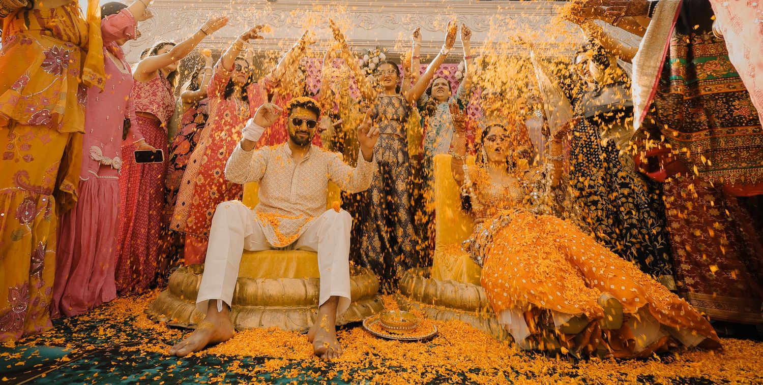A joyous celebration with yellow flower petals raining down during a traditional Indian wedding ceremony.