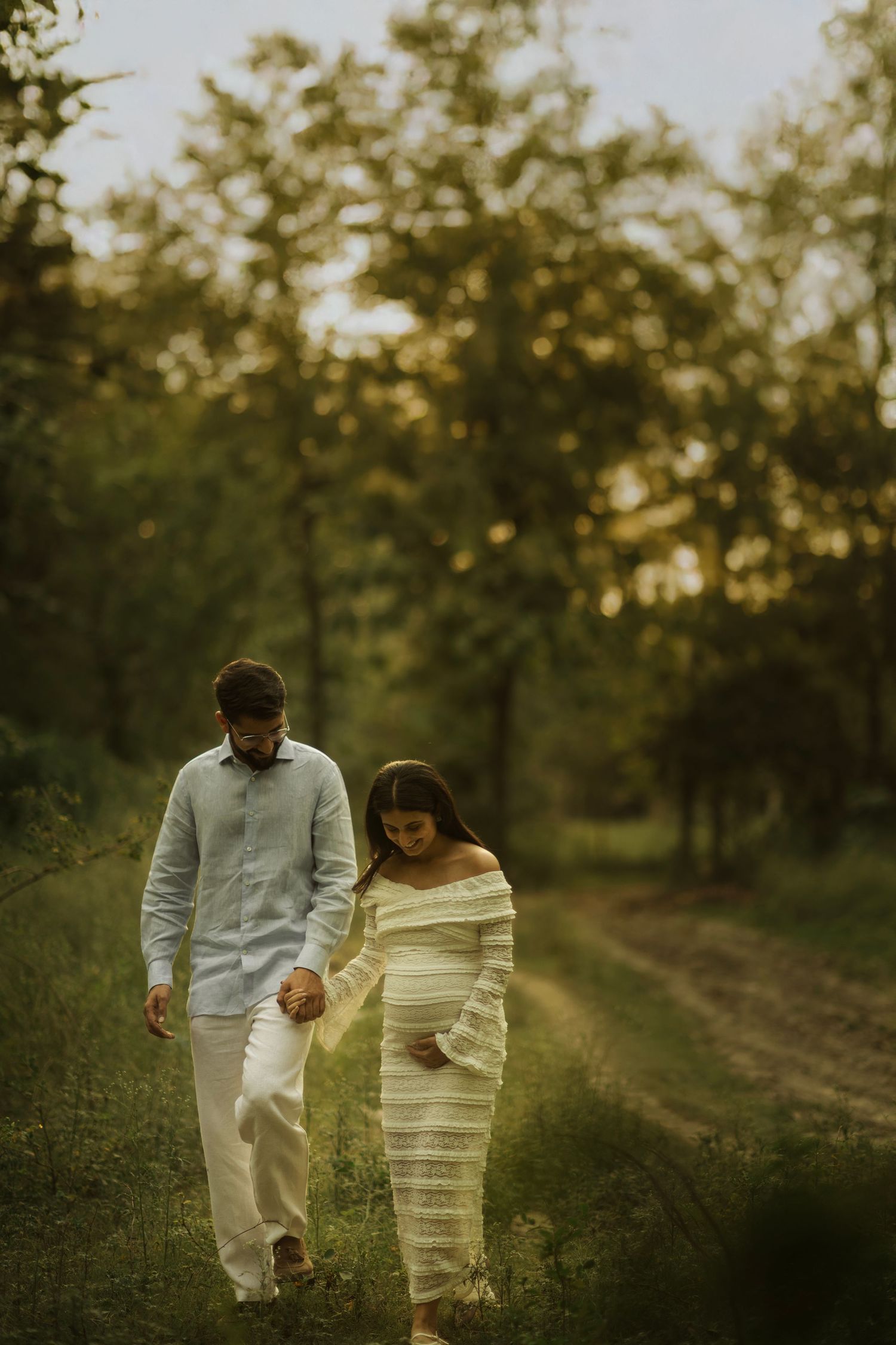 A couple walks hand in hand through a scenic orchard path during golden hour sunset.