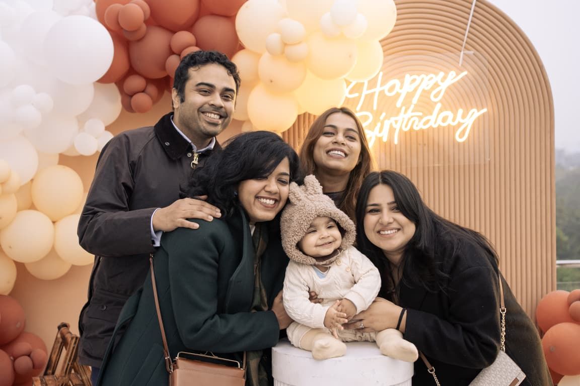 Family group photo at a birthday party with balloons and a Happy Birthday neon sign backdrop.