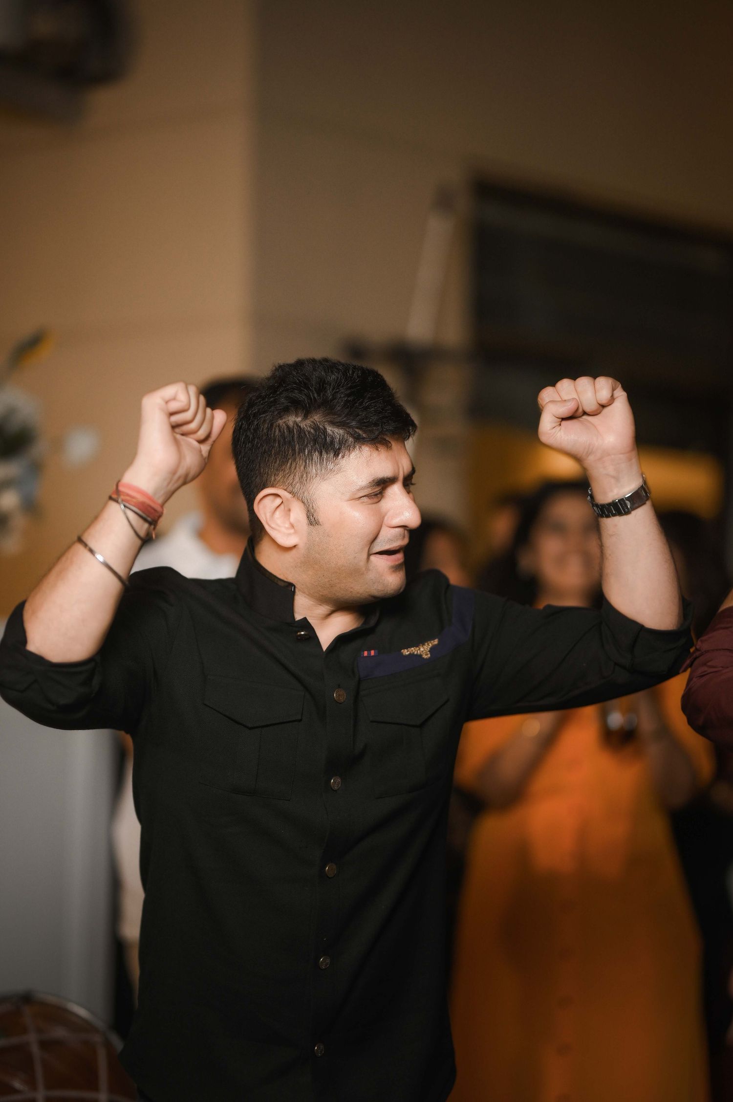 A man in a black shirt dancing with raised fists at an indoor celebration event.
