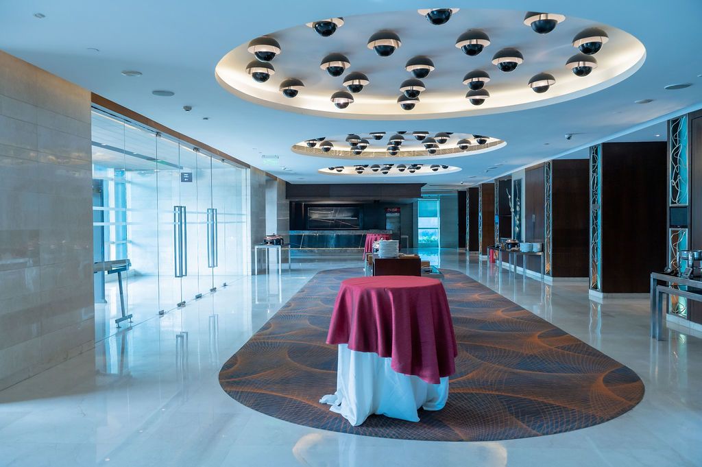 Elegant hotel lobby with marble floors, circular ceiling with pendant lights, and a draped round table centerpiece.