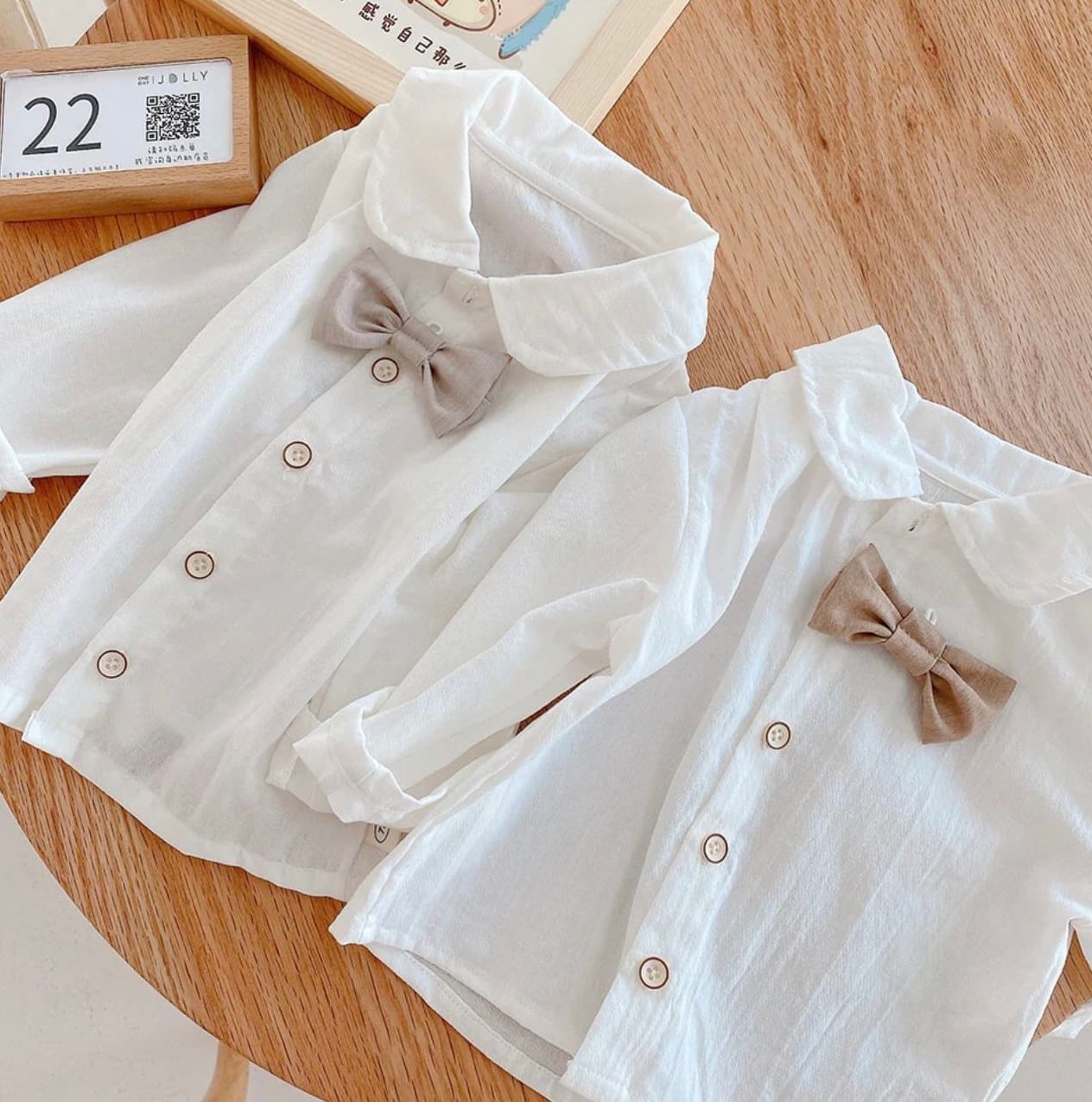 White linen baby dress with delicate puff sleeves and button details displayed on wooden surface.