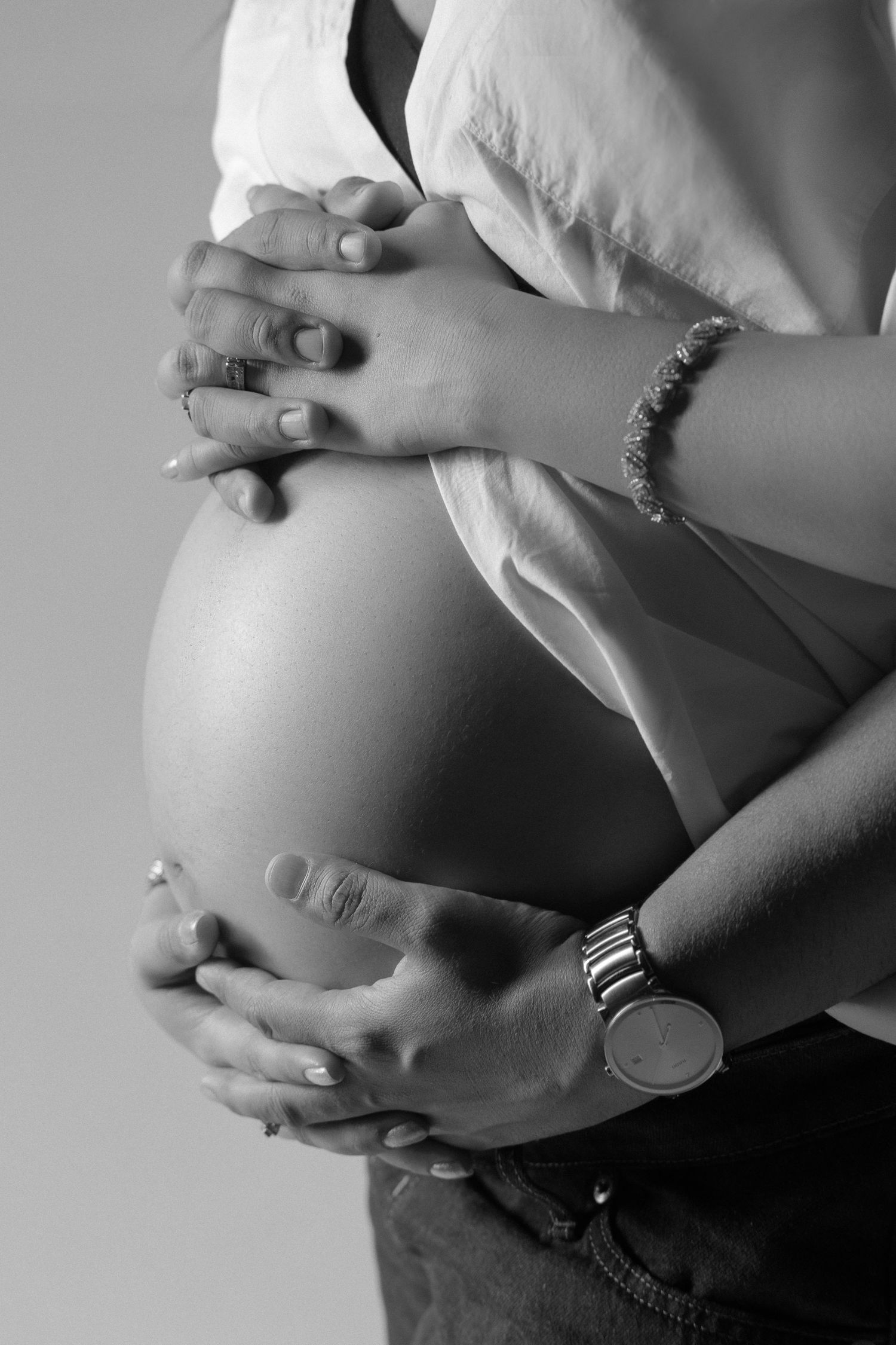 A black and white photo series showing a pregnant woman's belly being lovingly cradled from different angles.