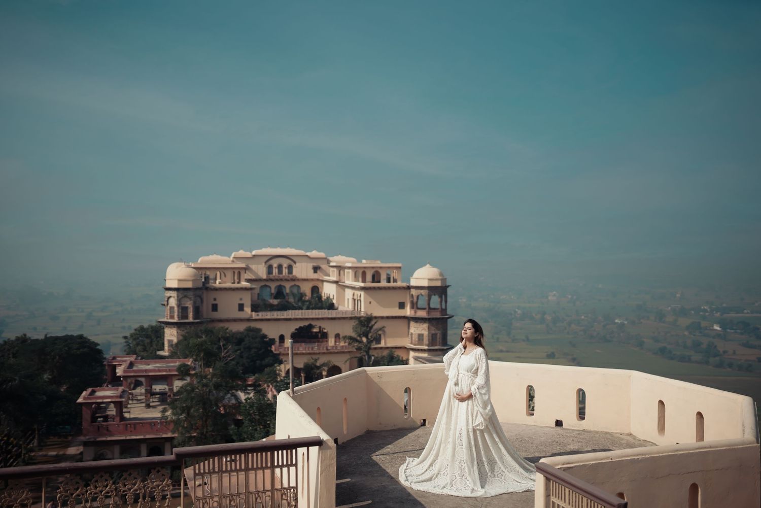 Bridal portrait on palace terrace overlooking cityscape with elegant white gown.
