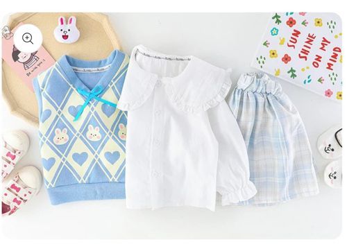 Three pieces of baby clothing including a blue patterned sweater, white shirt, and plaid shorts arranged on a light background.