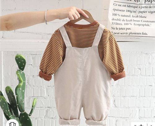 Neutral-colored baby clothes displayed against a white brick wall.