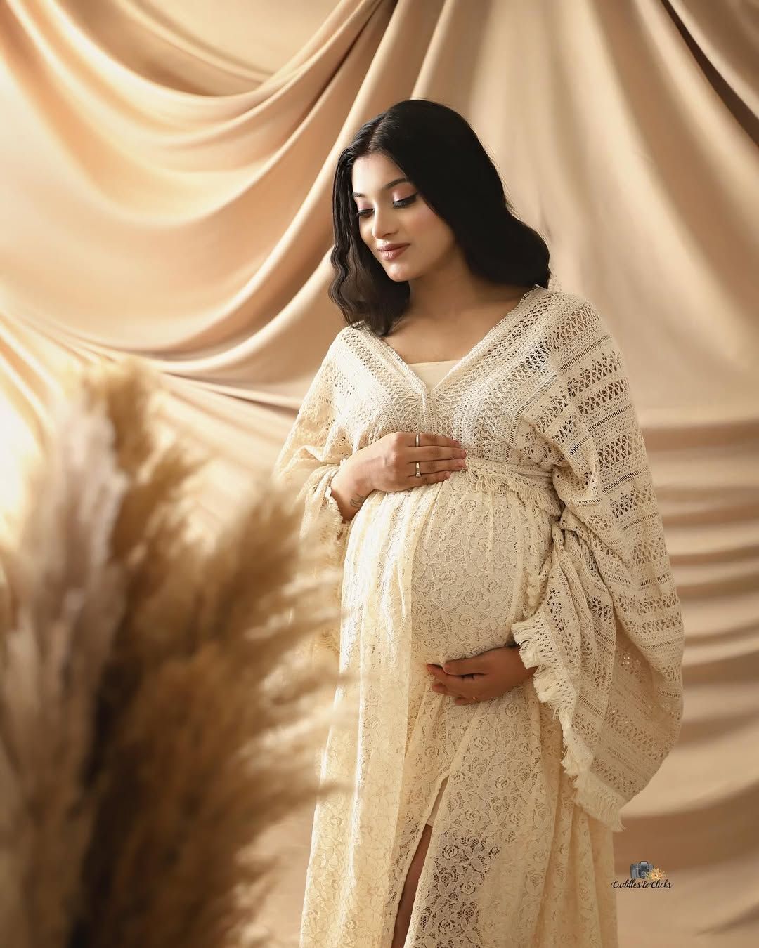 Serene maternity portrait in cream lace dress with draped fabric background.