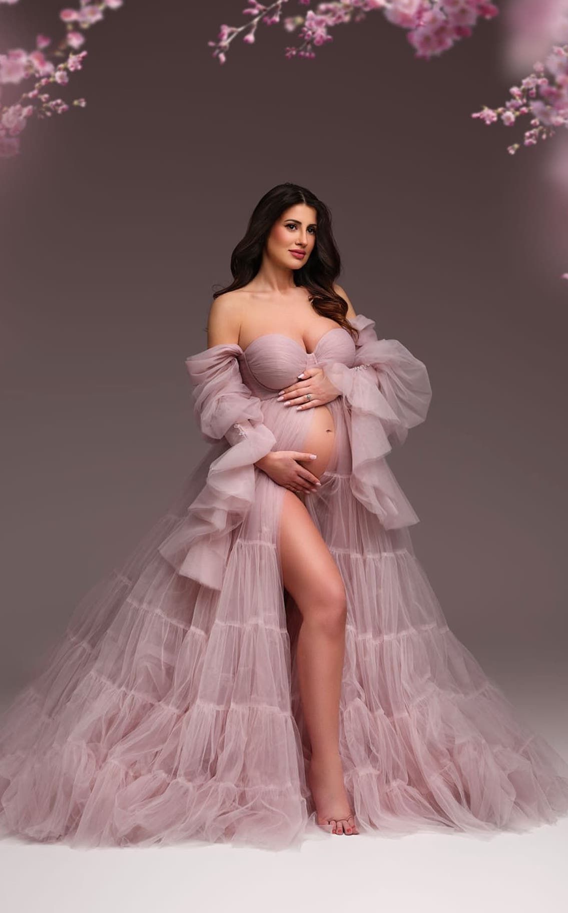 Pink maternity gown with cherry blossoms framing dramatic studio portrait.