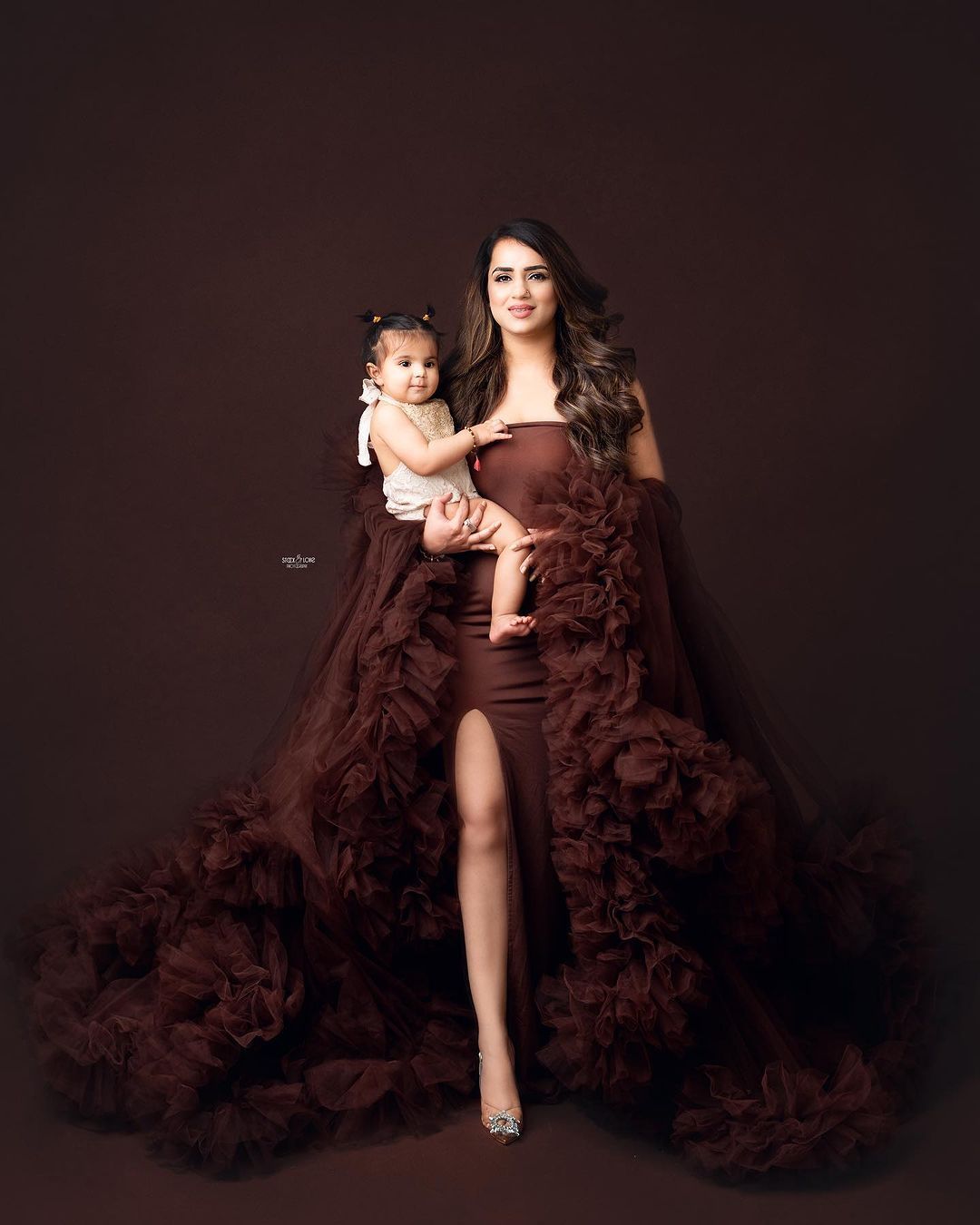 Artistic maternity portraits with dramatic burgundy ruffled gown against black background.