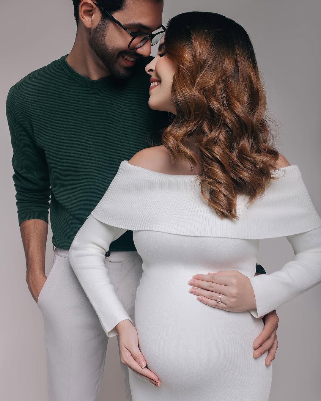 Intimate close-up of expecting couple in green and white sharing loving moment against gray background.