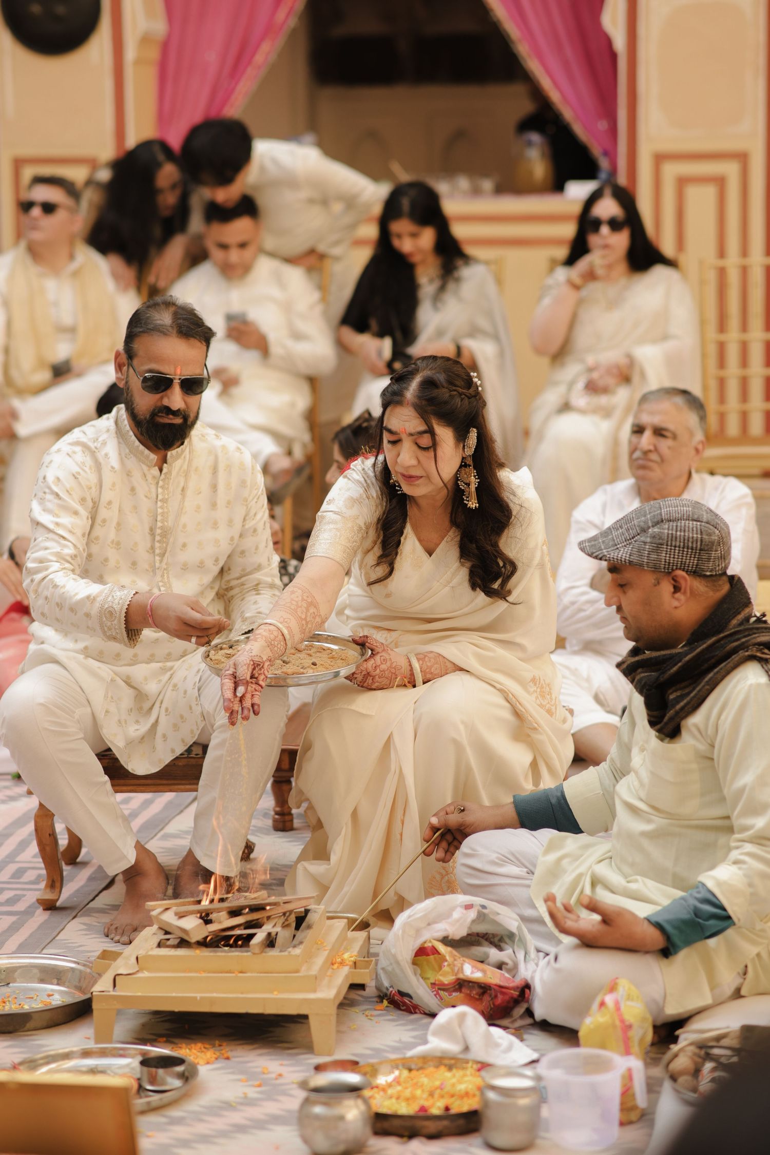 Traditional Indian wedding ceremony with guests seated on floor during ritual proceedings.