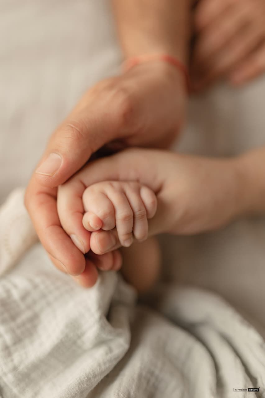 A parent gently holds a newborn baby's tiny hand, symbolizing love and new life.