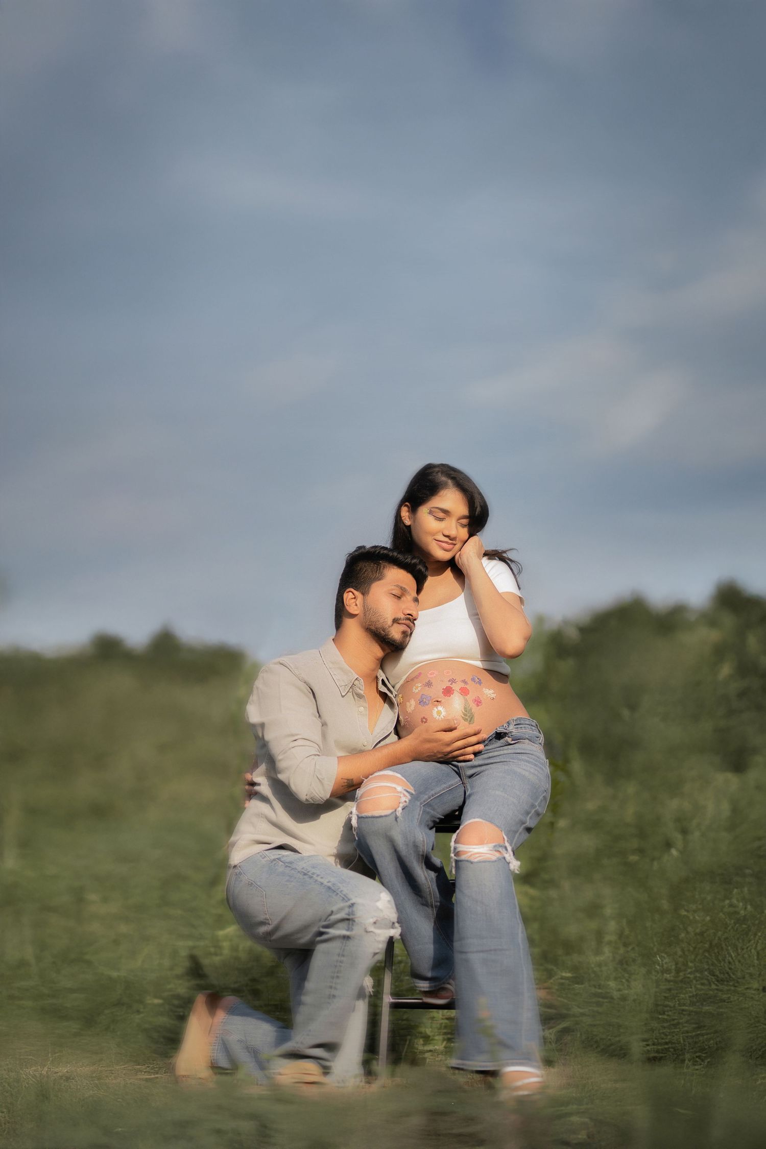 Expecting couple embraces in a grassy field under a moody sky during maternity photoshoot.