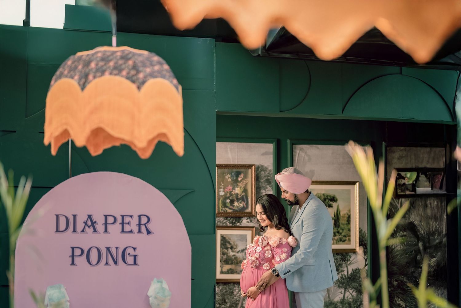 Couple embracing at a baby shower with a colorful Diaper Pong game sign against a green backdrop.