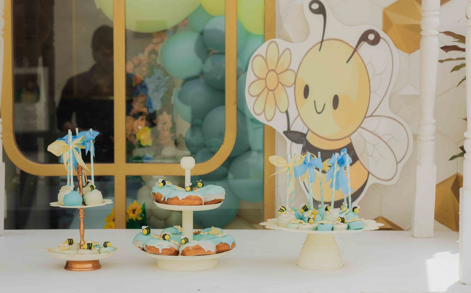 Bee-themed birthday party dessert table with cupcakes, cake pops, and a cute bumblebee decoration in soft blue and gold tones.