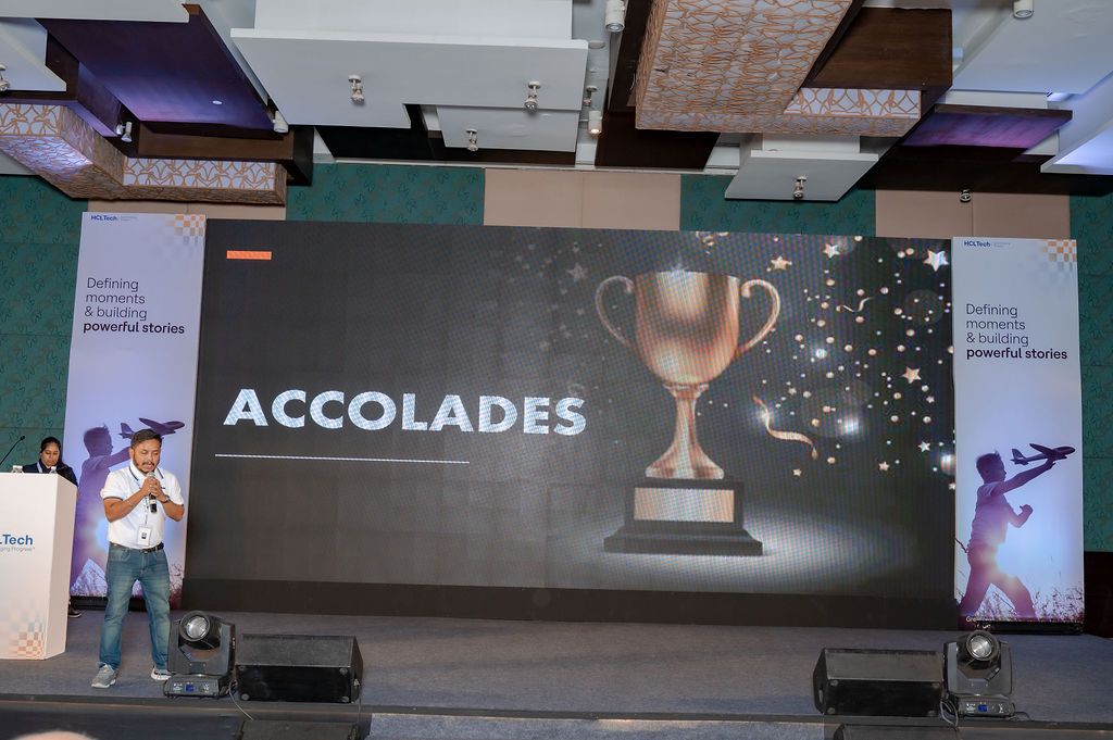 A stage presentation screen displays 'ACCOLADES' text with a trophy graphic and sparkles against a dark background.