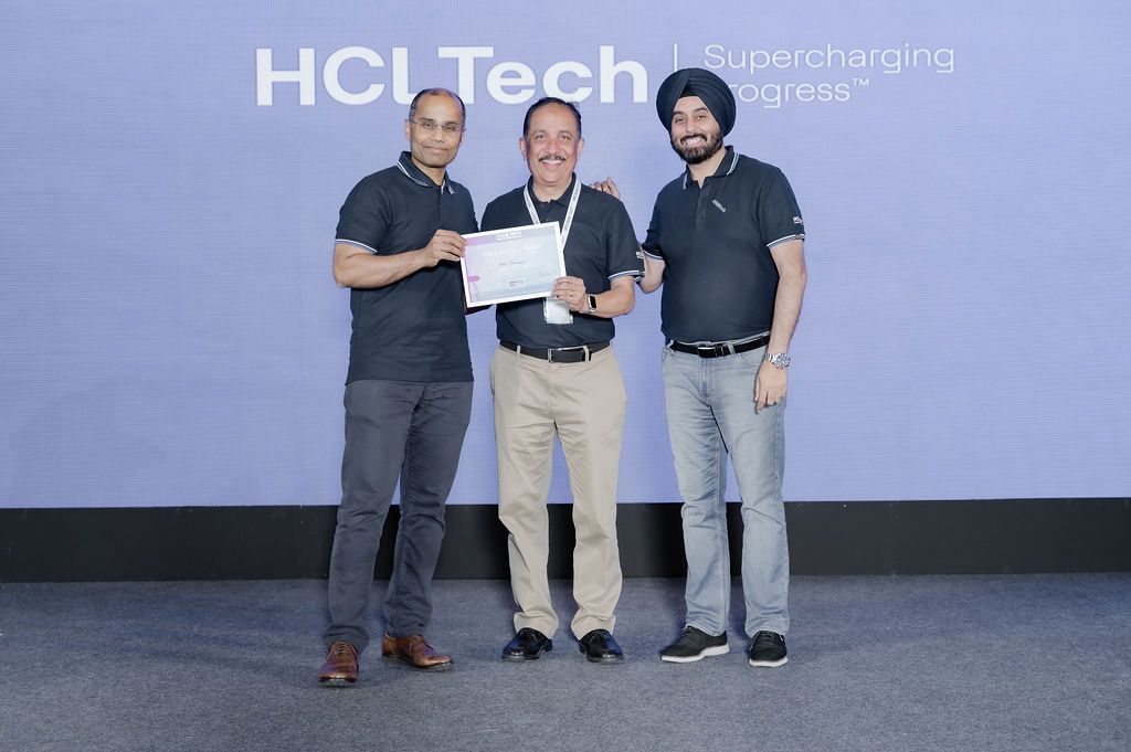 Group of people in business casual attire standing together against a gray wall during a tech event.