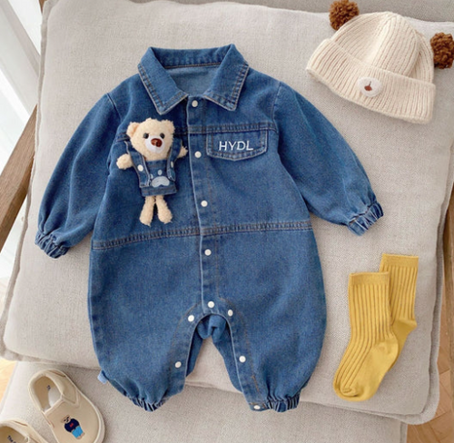 Close-up of denim baby outfit with stuffed teddy bear pin attached to chest pocket.