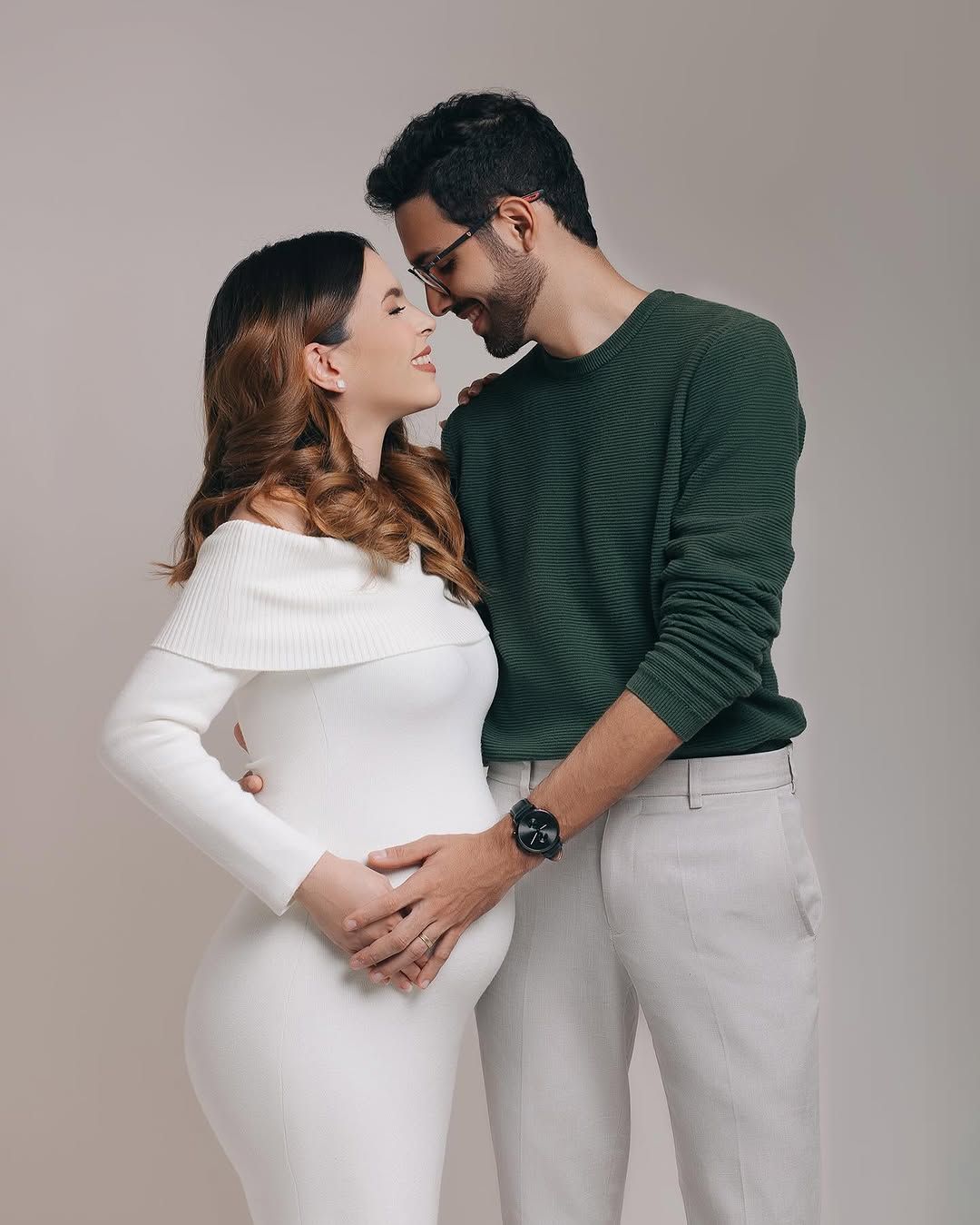 Intimate maternity photo of couple in white dress and green sweater sharing tender moment.