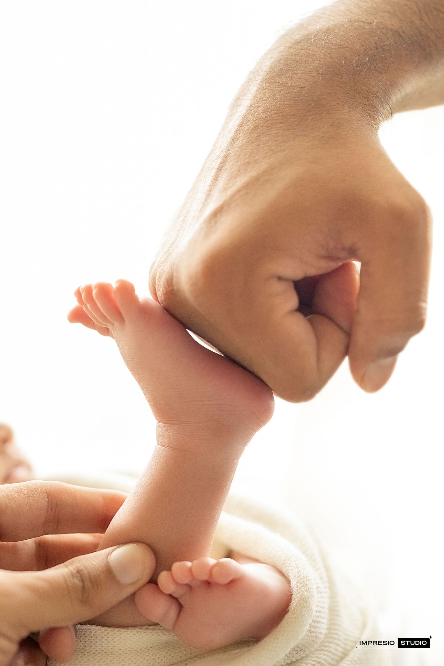 Close-up of a newborn baby's tiny feet held gently by adult hands against a white background.