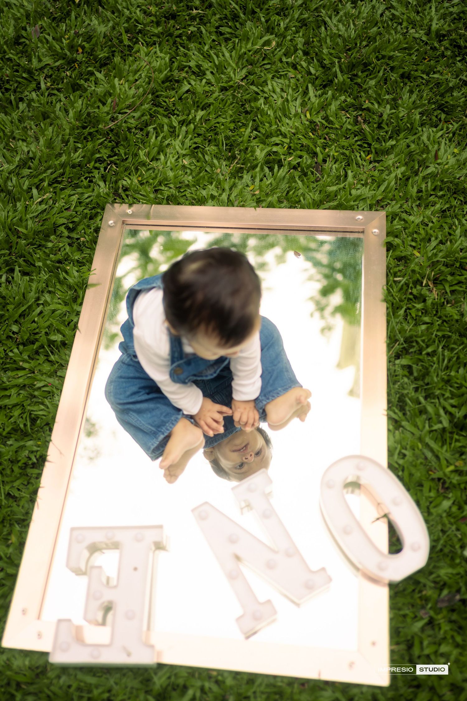 A sequence of photos showing someone drawing on a large piece of paper while sitting on green grass outdoors.