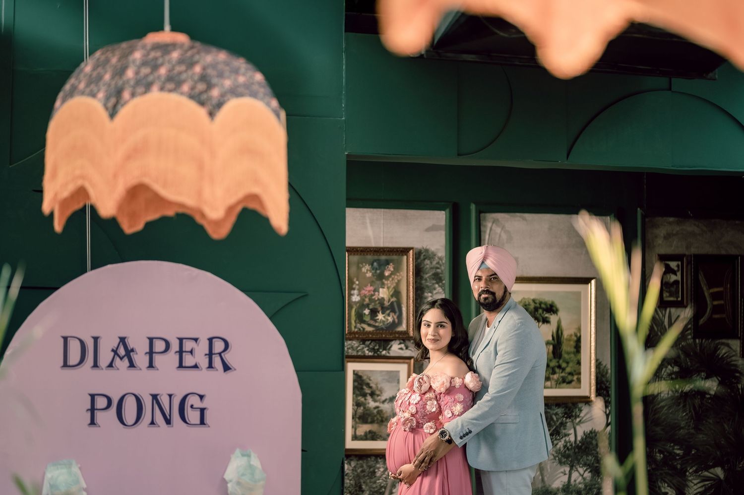 Couple posing at a baby shower with a Diaper Pong sign against a green backdrop.