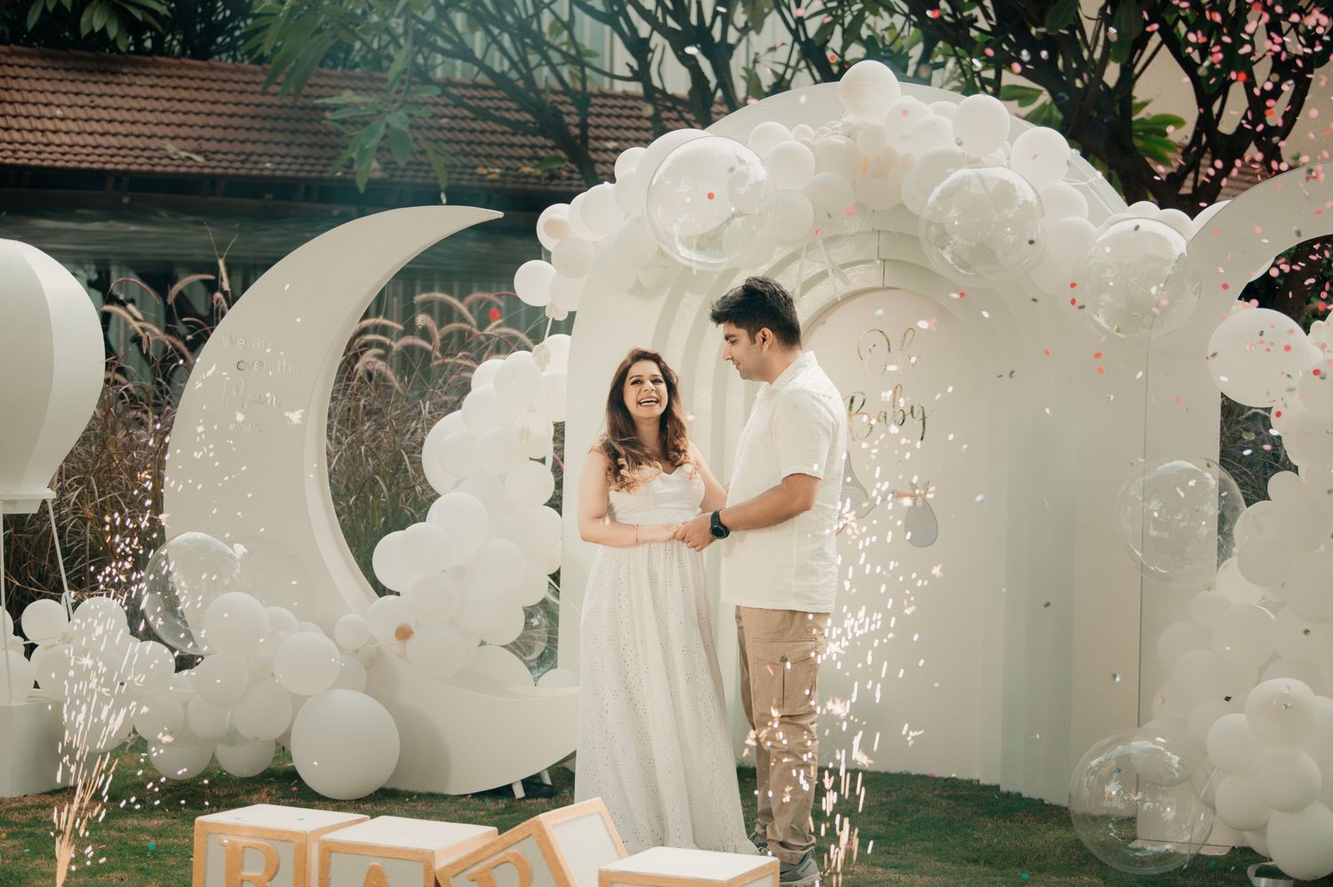 Couple standing under white balloon arch with moon decor at an outdoor celebration event.