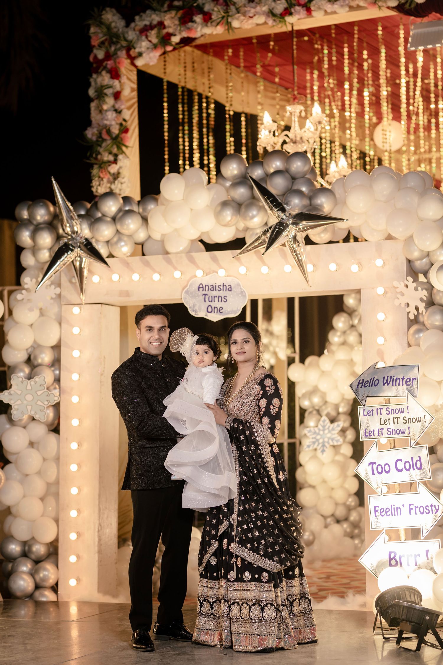 Family posing at a winter-themed first birthday party with balloon arch, star decorations, and festive signage.