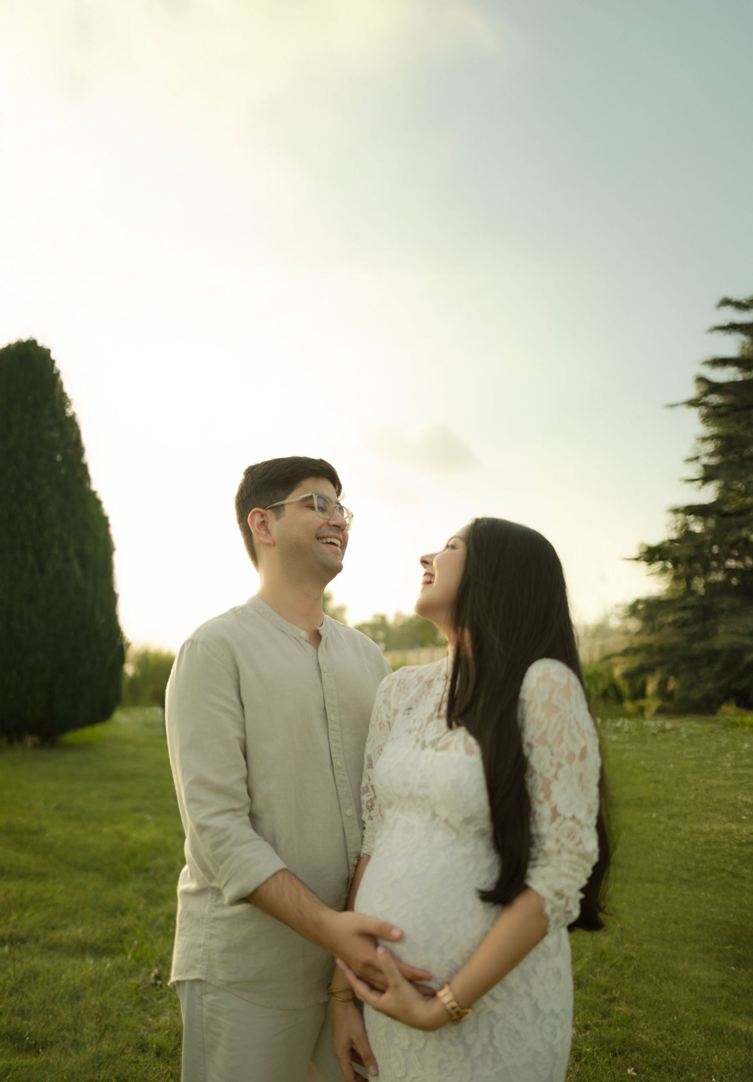 A couple shares intimate moments in a sunny field at sunset wearing white outfits.