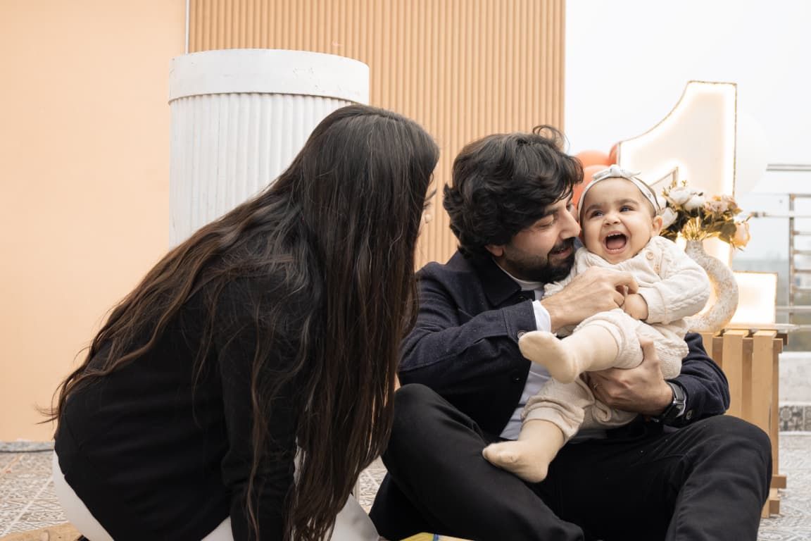 Happy family with parents and laughing baby in festive Christmas outfit sitting together indoors.