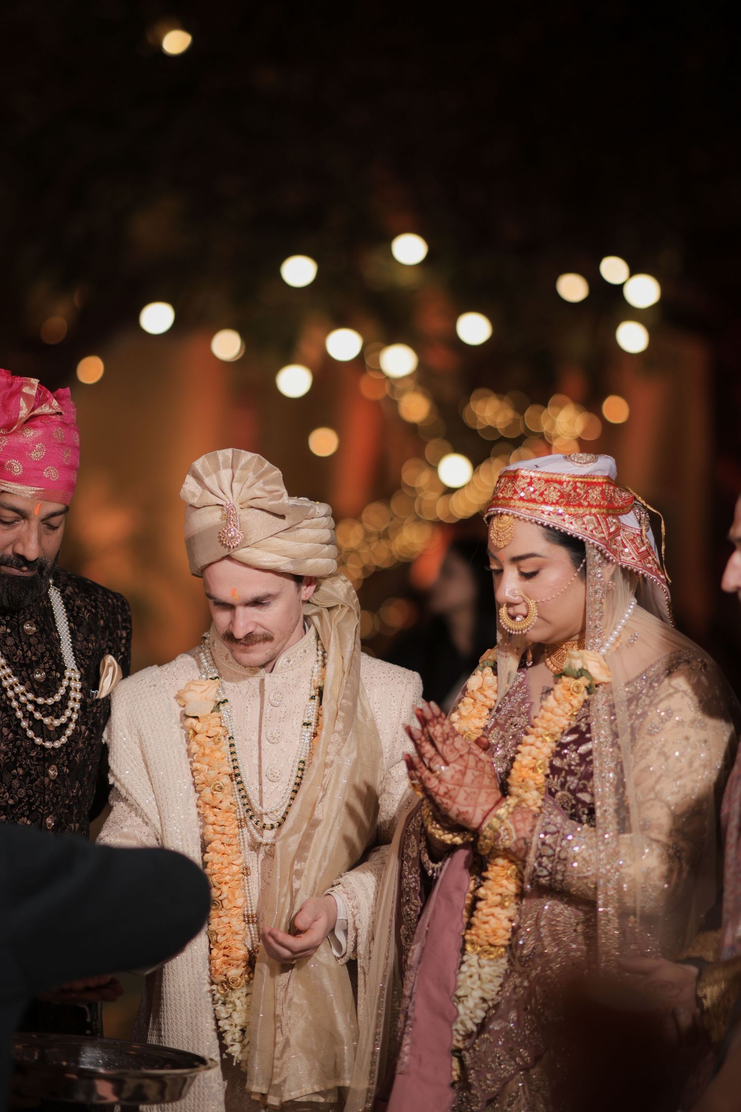 Traditional Indian wedding ceremony captured in warm lighting with guests wearing elegant traditional attire and floral garlands.