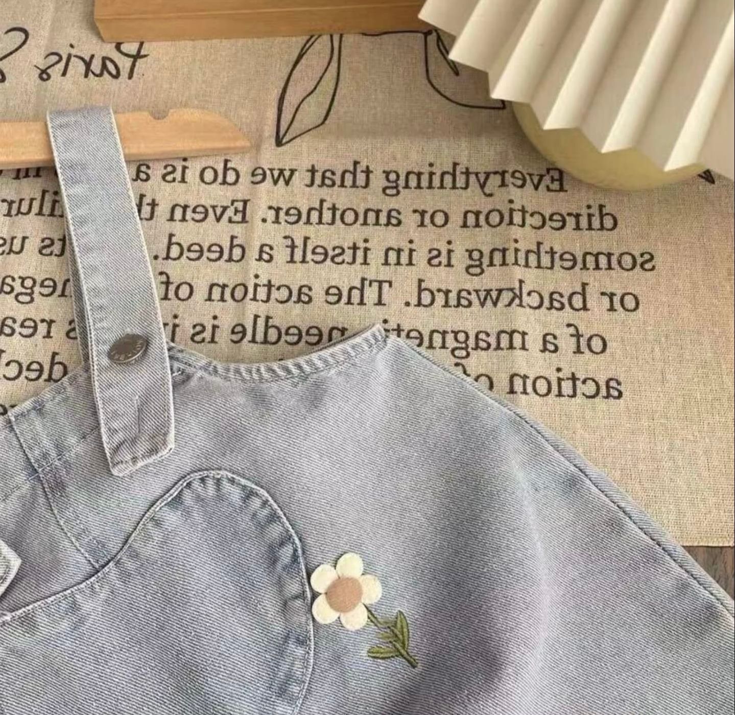 A light gray denim jacket collar with floral embroidery detail shown against a textured beige background.