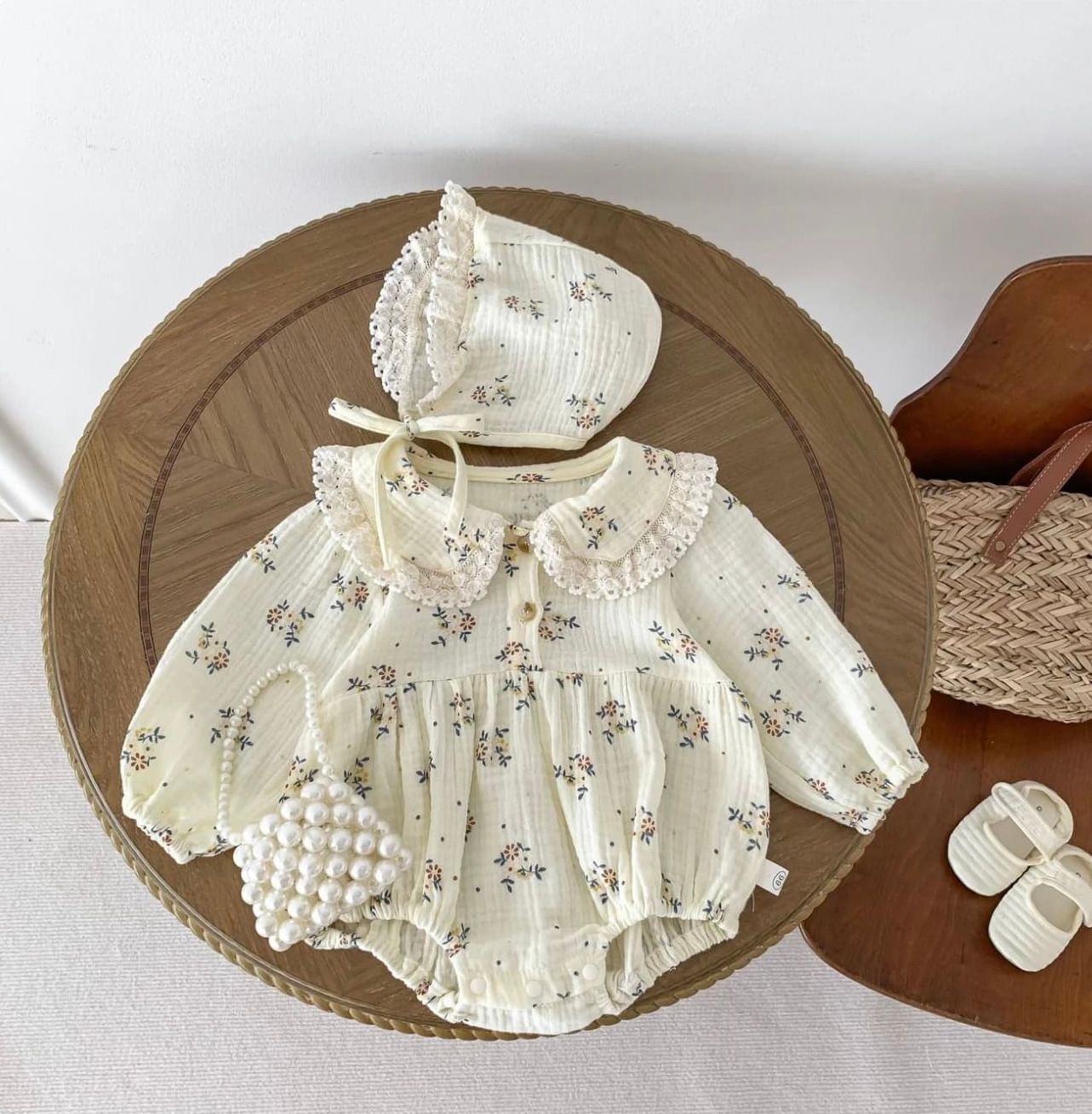 Vintage-style baby dress in white cotton with delicate floral print and ruffled details laid out flat for display.