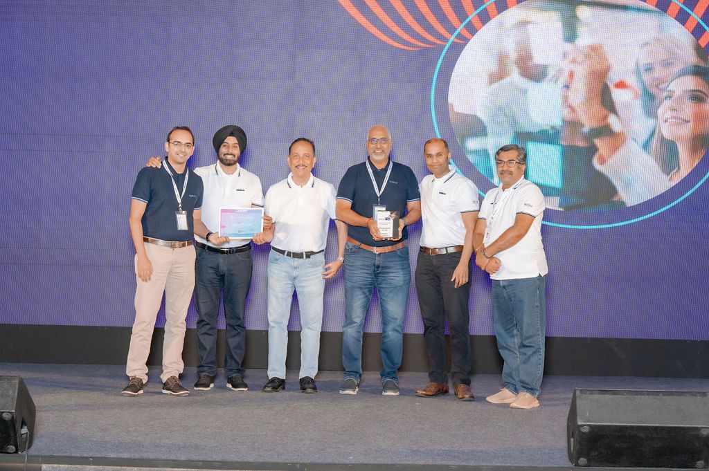 Group of six professionals on stage receiving awards at a corporate event with colorful backdrop.