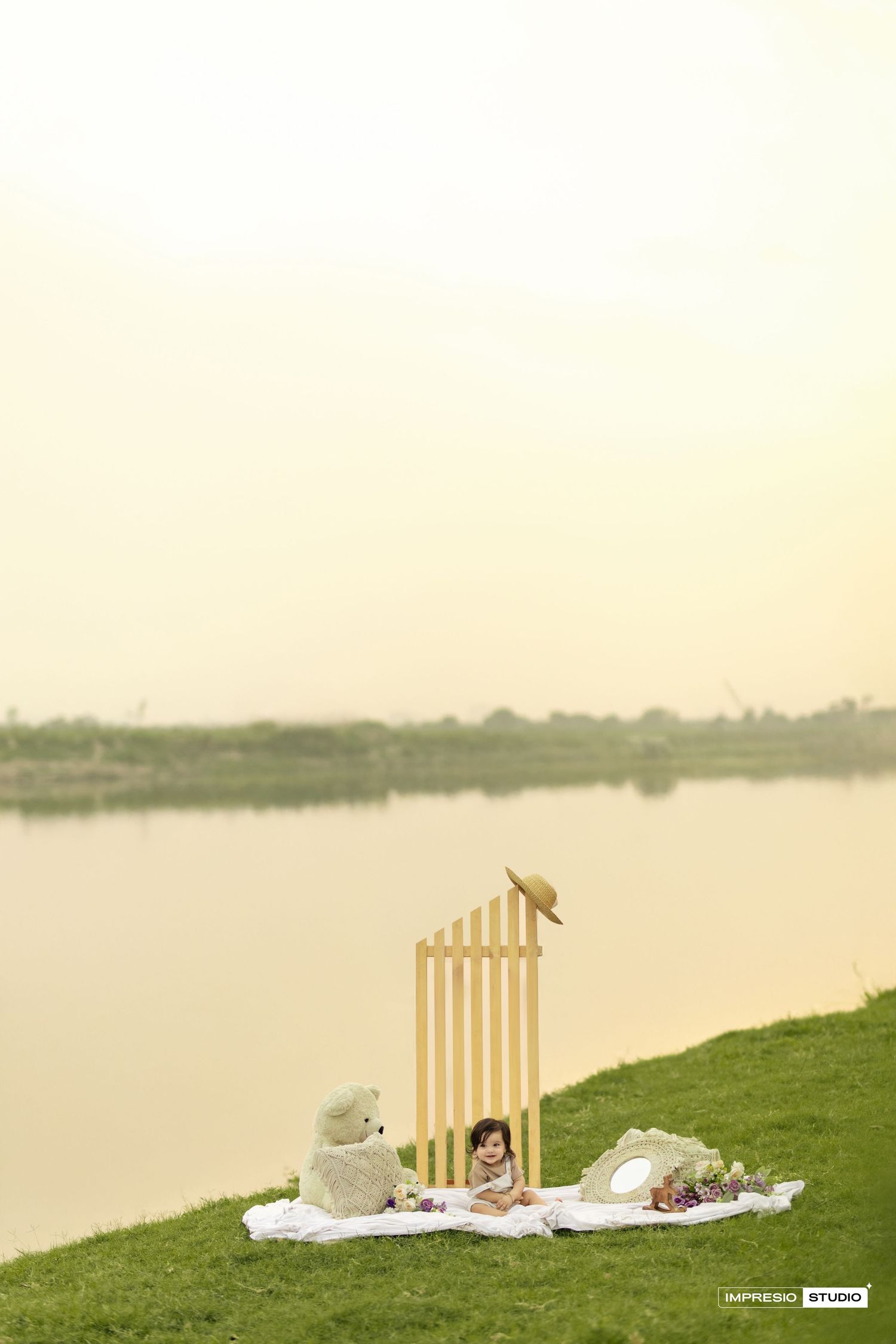 Peaceful lakeside picnic setup with wooden chairs and blankets on grassy shore during golden hour.