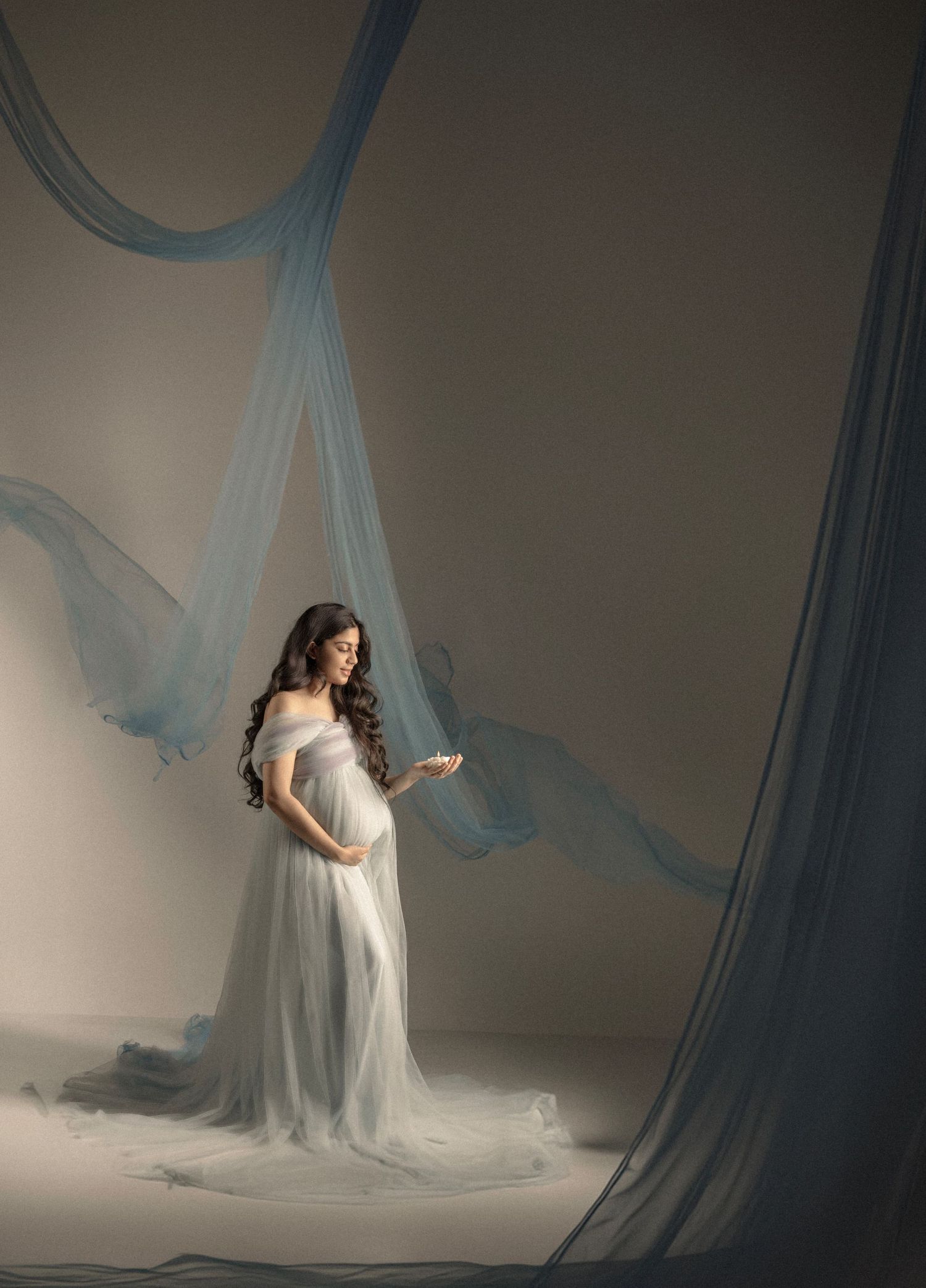 Studio maternity session with draped blue fabric creating ethereal atmosphere.