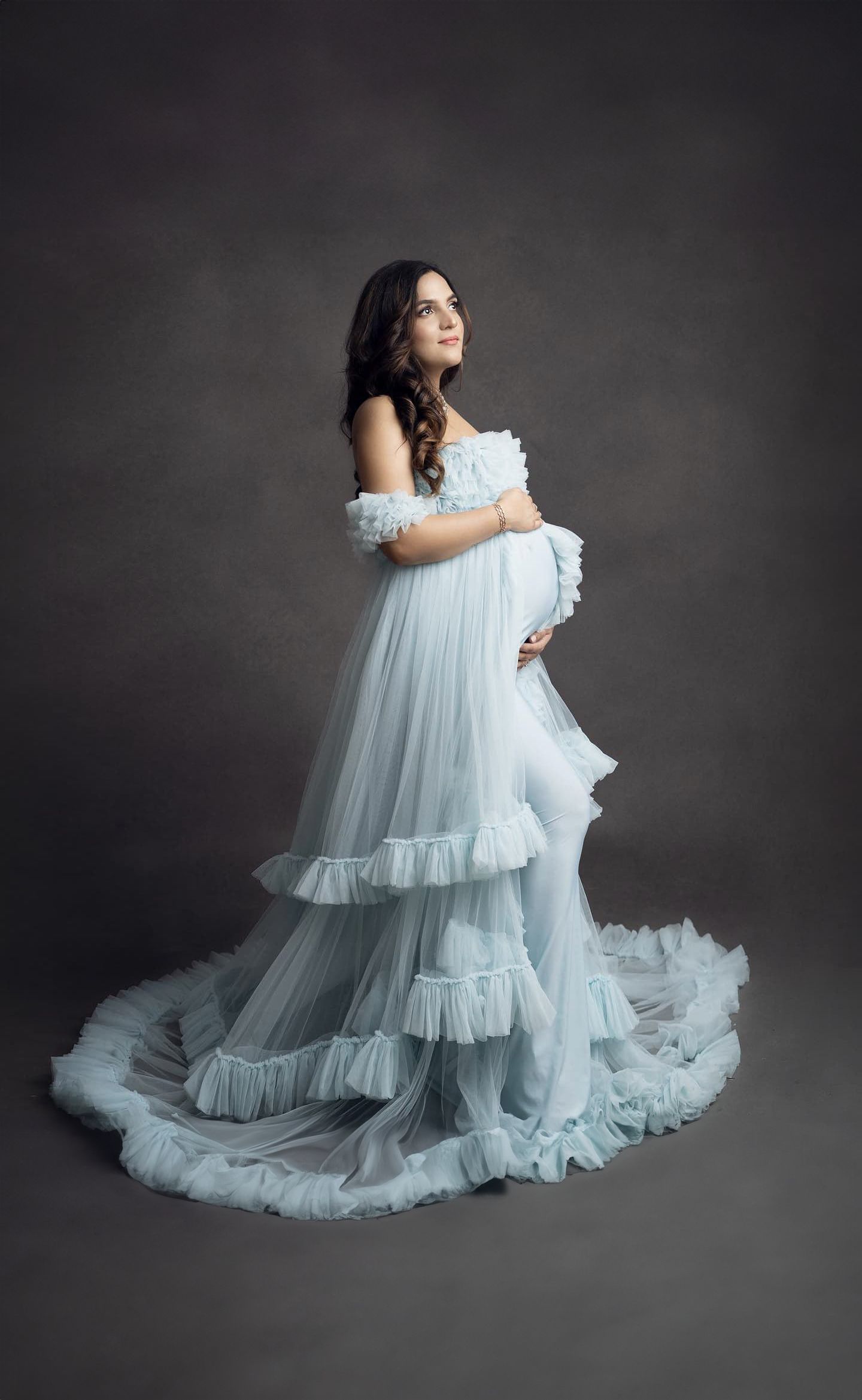 Ethereal maternity portraits featuring a billowing pale blue tulle dress on a dark background.