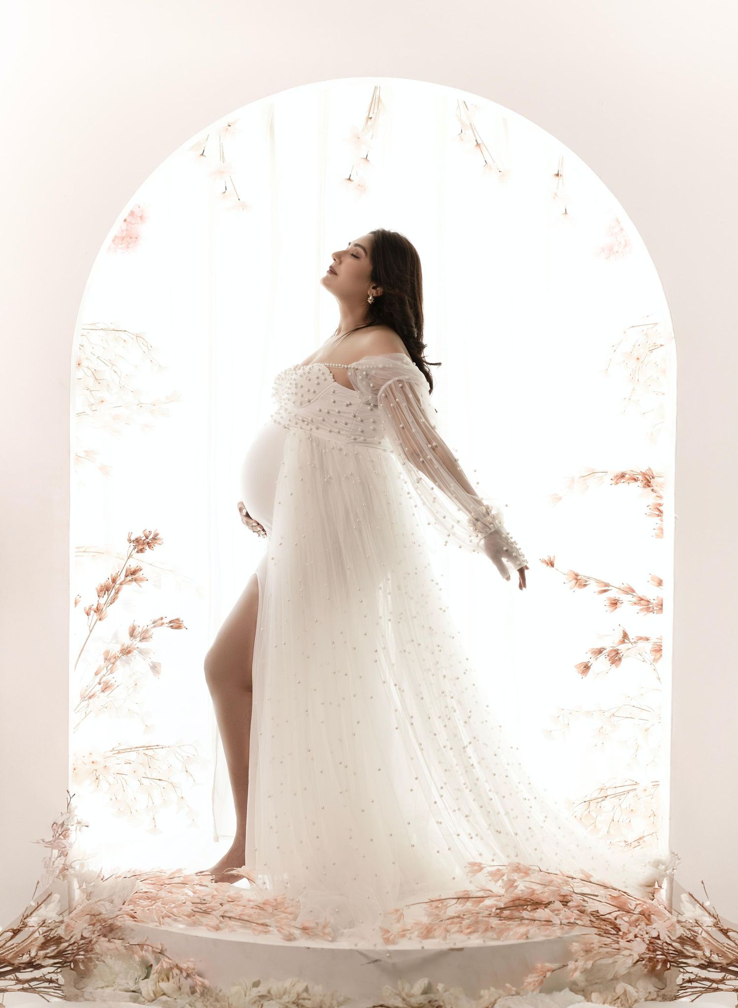 Artistic maternity photo featuring a white lace dress in an arched doorway with soft lighting.