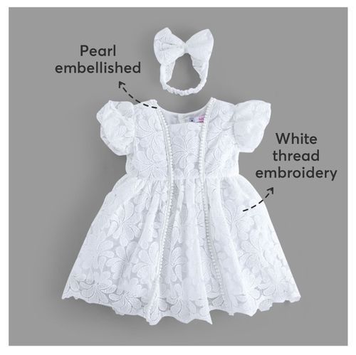 White christening dress with pearl details, bow headband, and embroidery shown with labeled features.