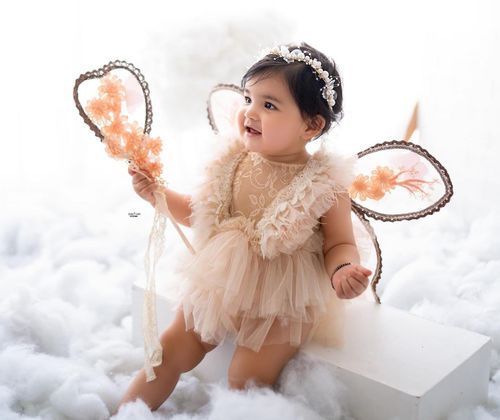 Adorable baby girl wearing peach tulle dress poses on soft white backdrop creating dreamy professional portraits.