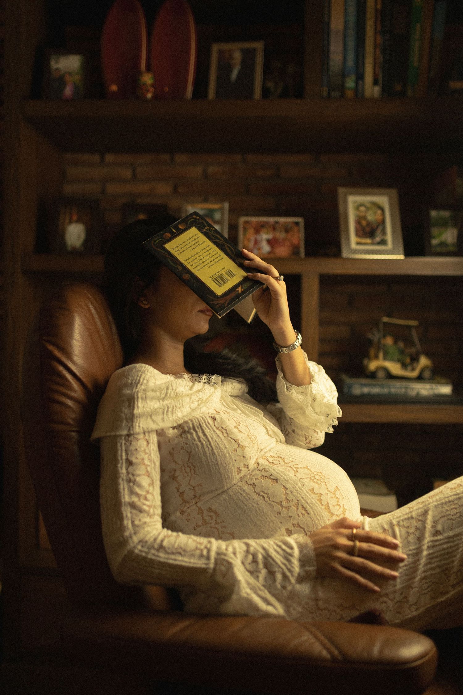A person in white lace reclining with books in a cozy library setting with warm lighting.