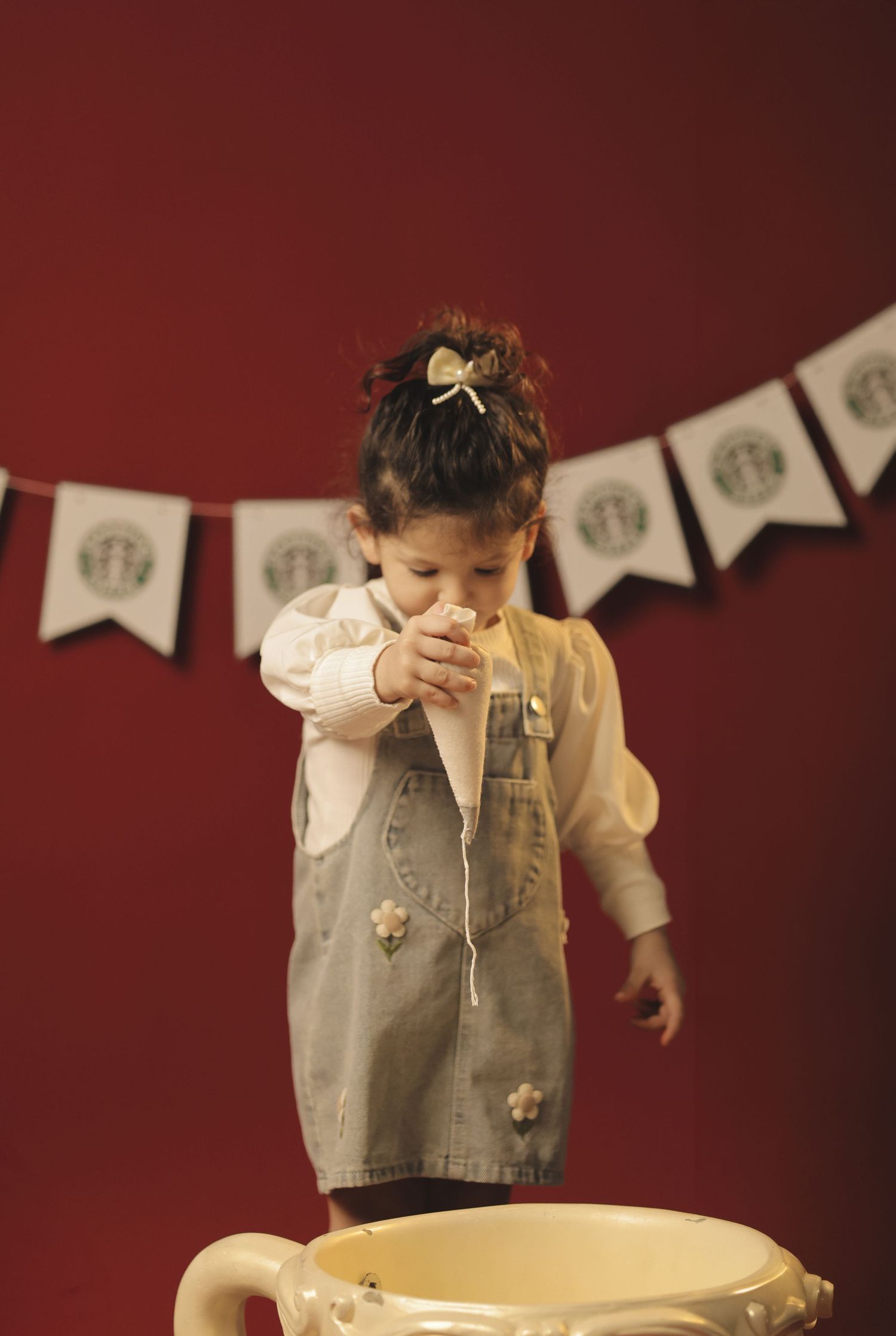 Toddler girl in denim dress standing in oversized teacup at Starbucks-themed birthday party.