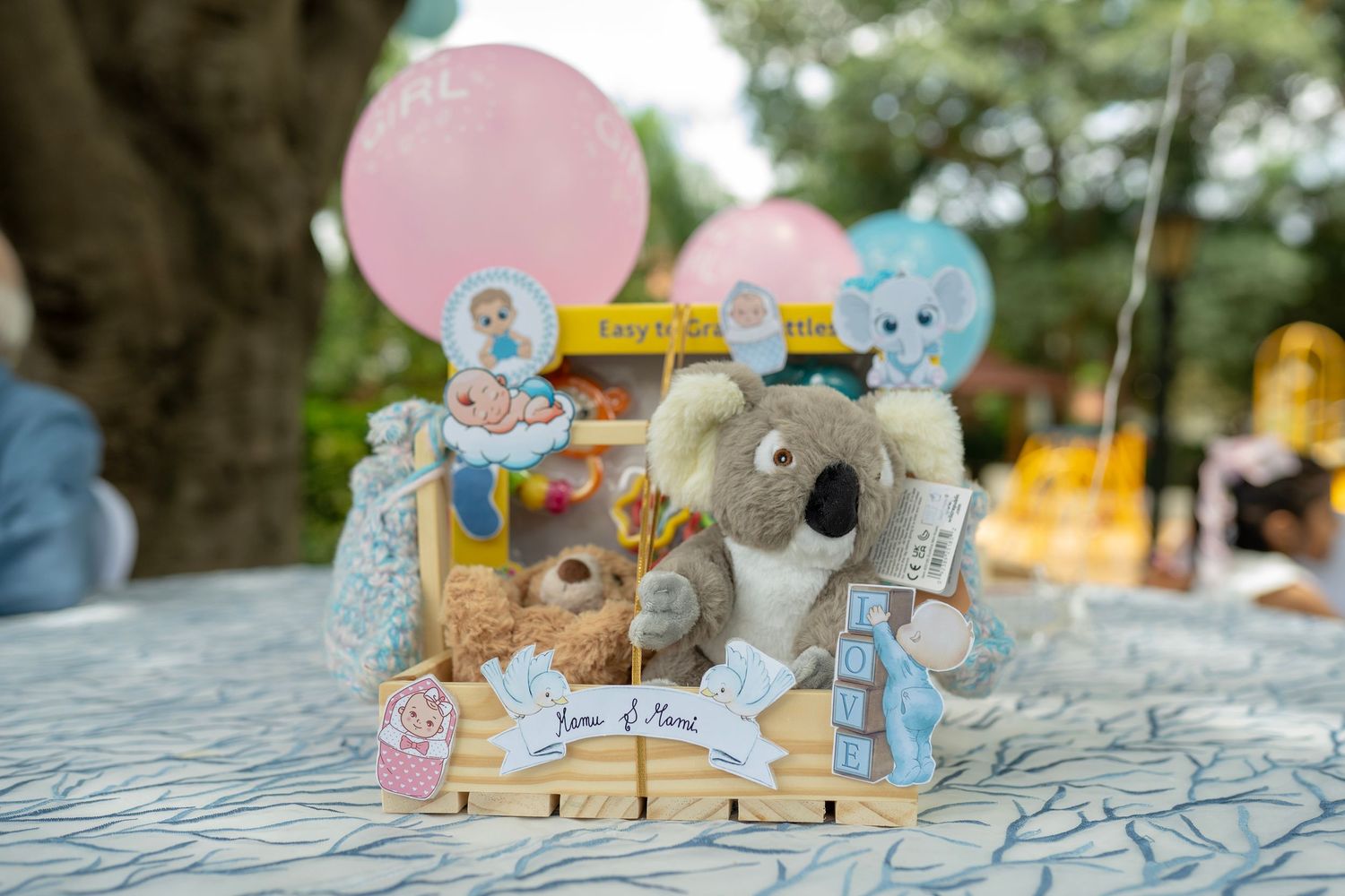 Baby shower centerpiece with koala plush, storybook characters, pink balloon, and personalized name signs on a decorated table.