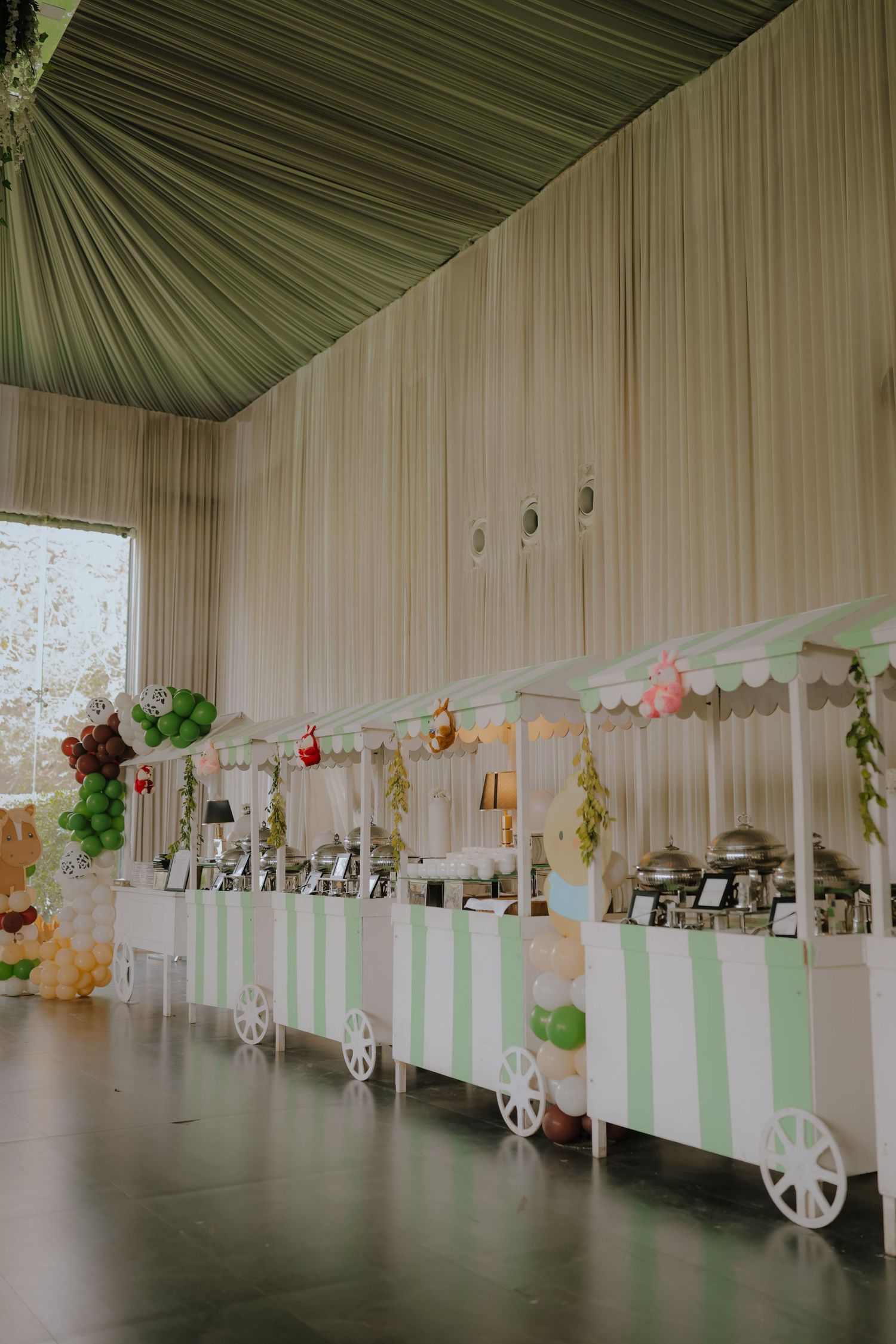 Green and white striped candy cart display with balloon decorations in an elegant draped event venue.