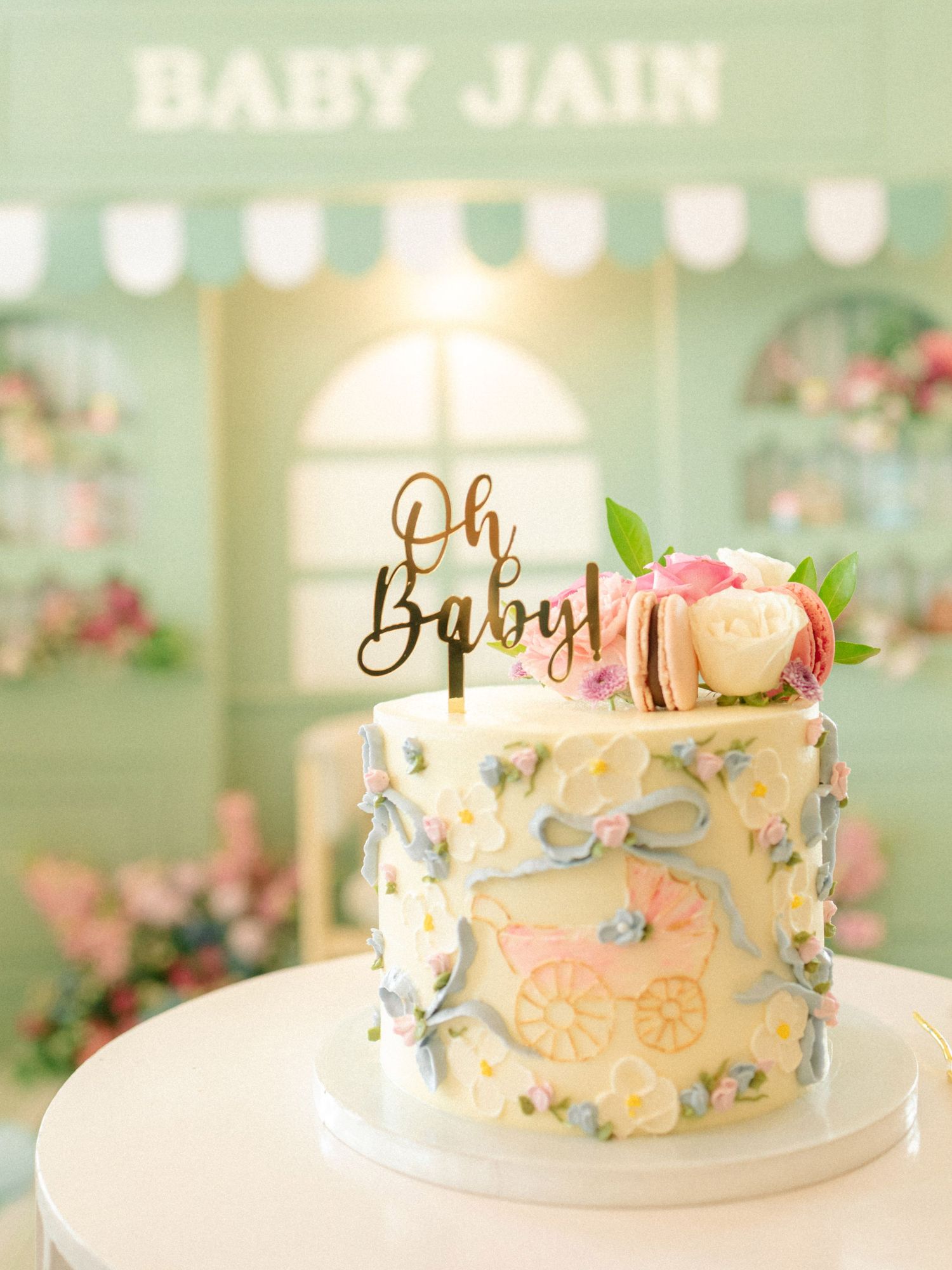 Elegant baby shower cake with floral decor, baby carriage design, and Oh Baby gold topper at Baby Jain celebration.