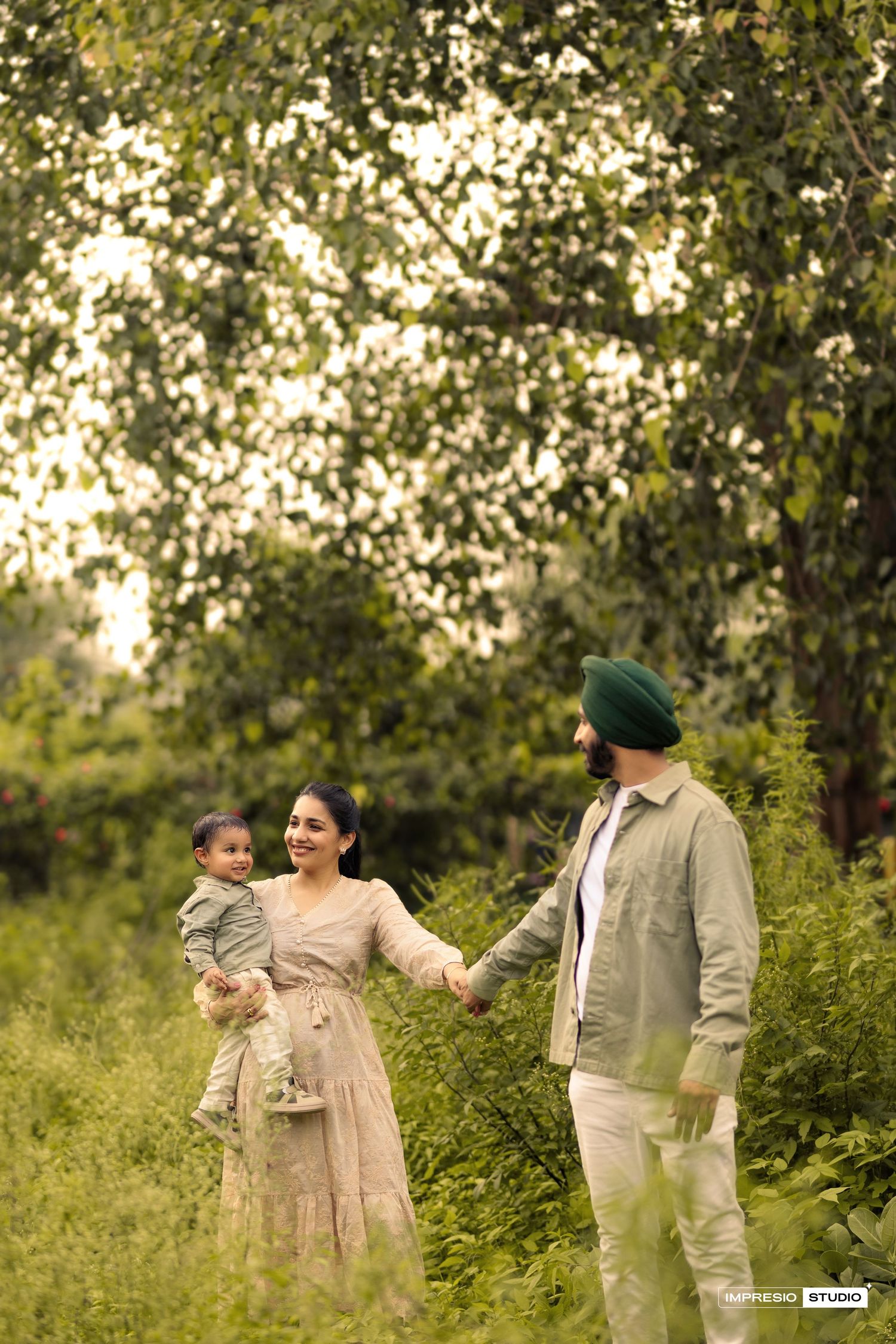 A family in coordinated beige outfits walks together through a sunlit garden with green foliage in the background.
