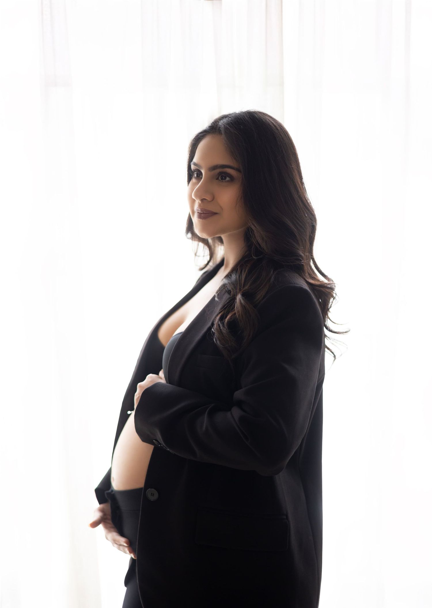 Elegant maternity portrait in business attire with natural window lighting.