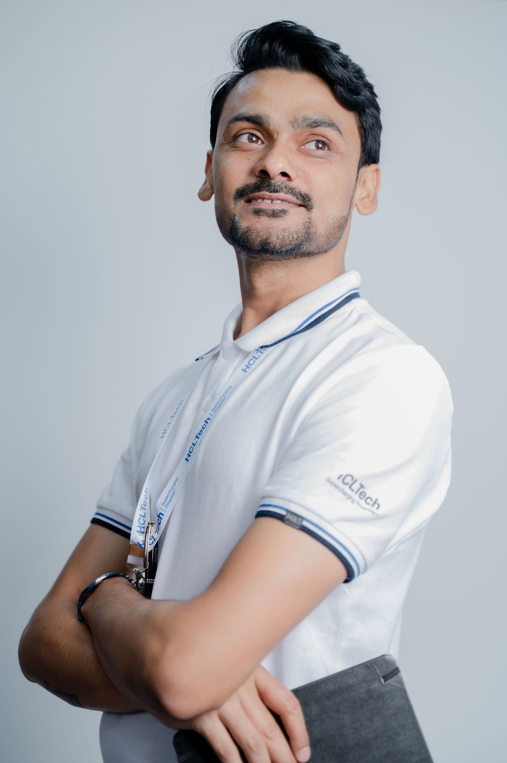 Professional man in white IQLTech polo shirt with arms crossed, looking upward confidently against gray background.