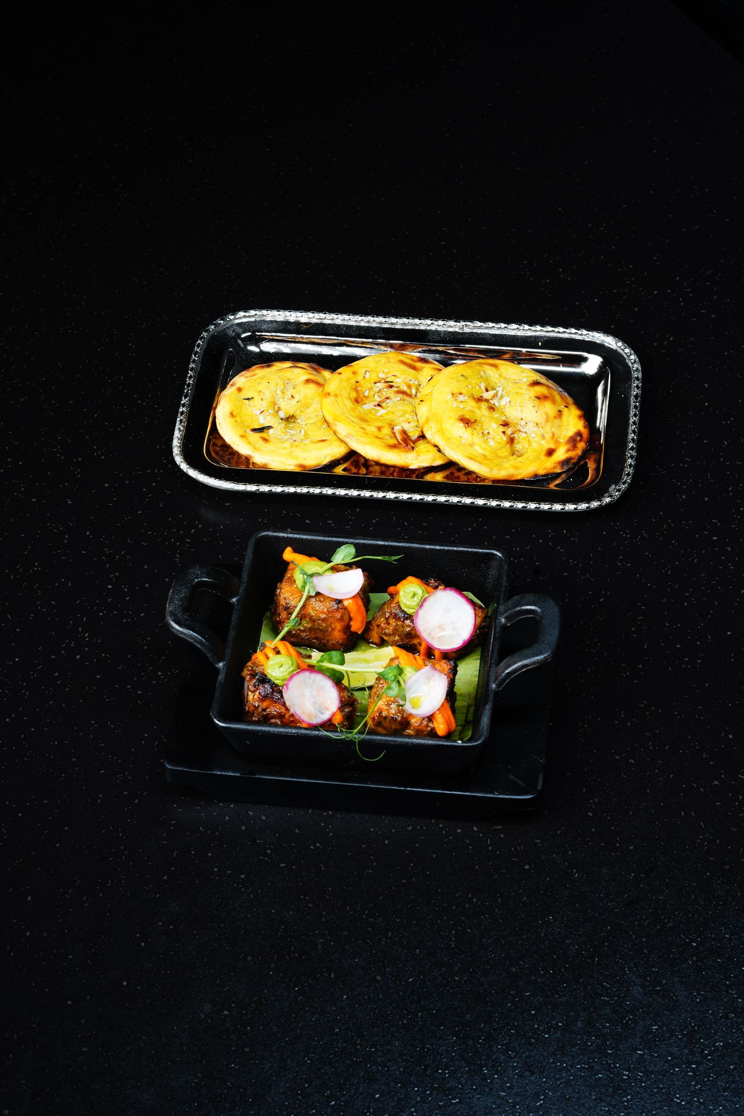 Crispy flatbreads served alongside colorful salad with radishes in black serving dishes.