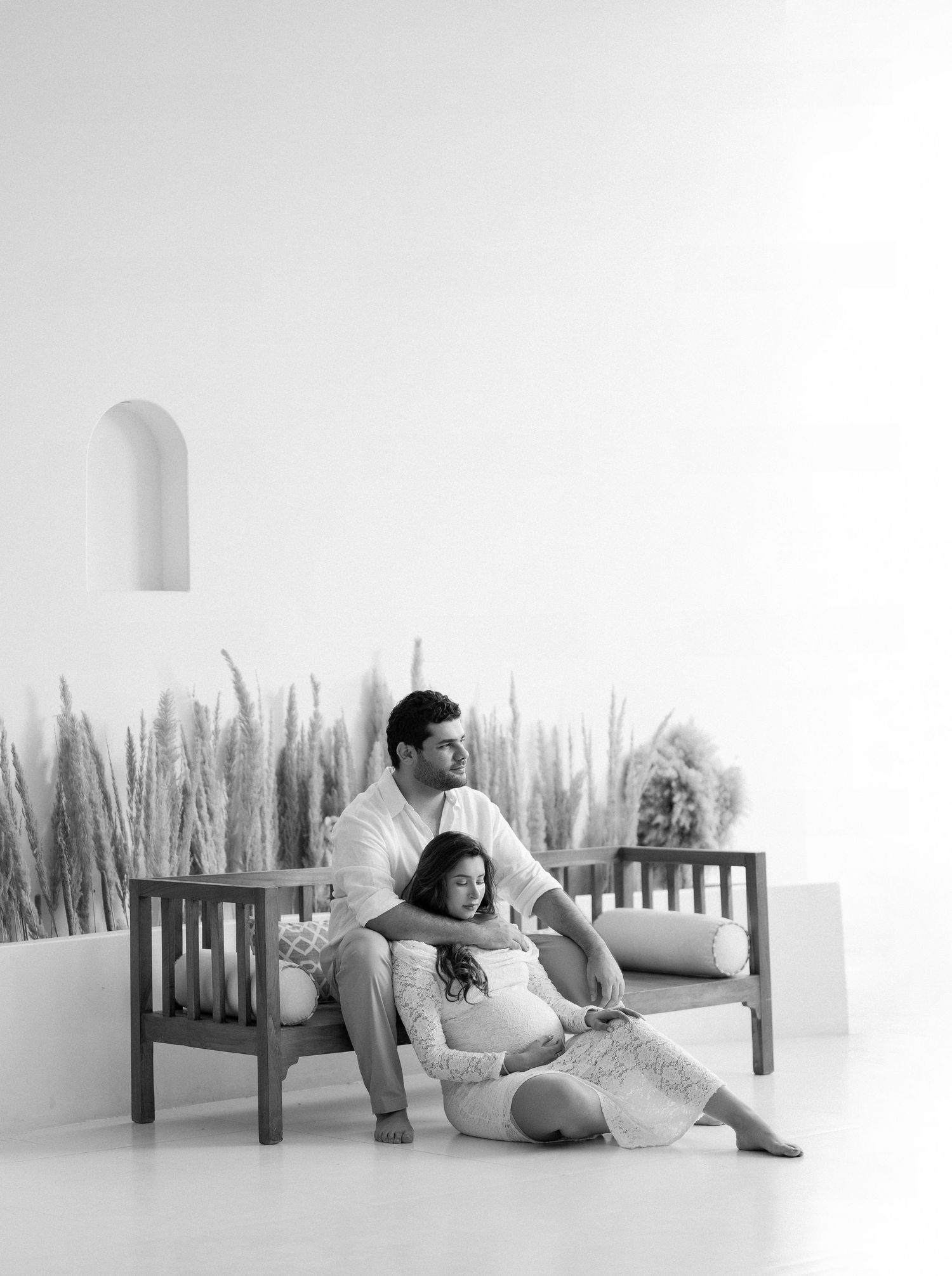 A couple in white clothing sits on a white floor in a minimalist setting with a series of romantic poses.